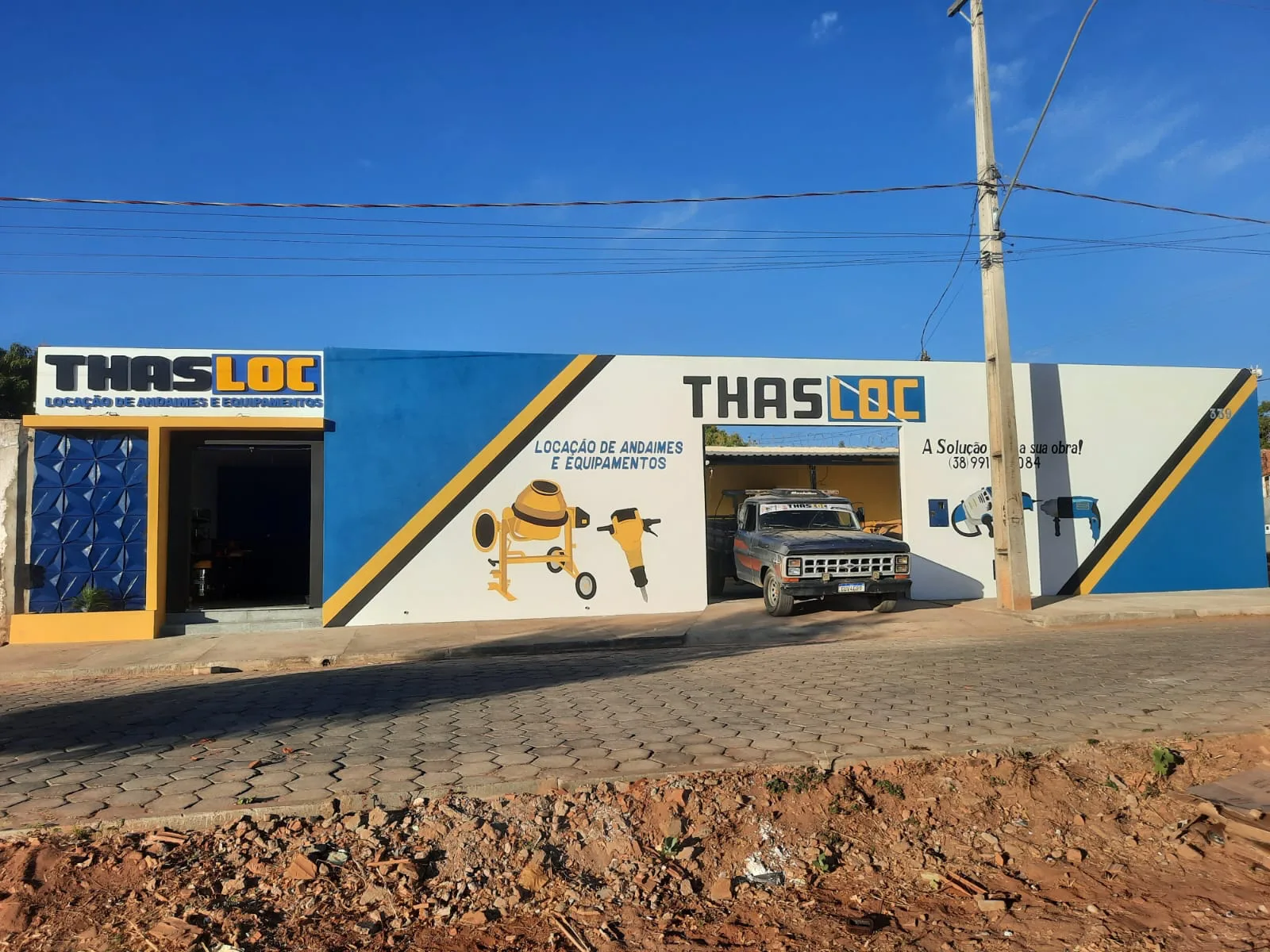 Fachada da loja THASLOC, com a pintura azul e amarela e a caminhonete na entrada